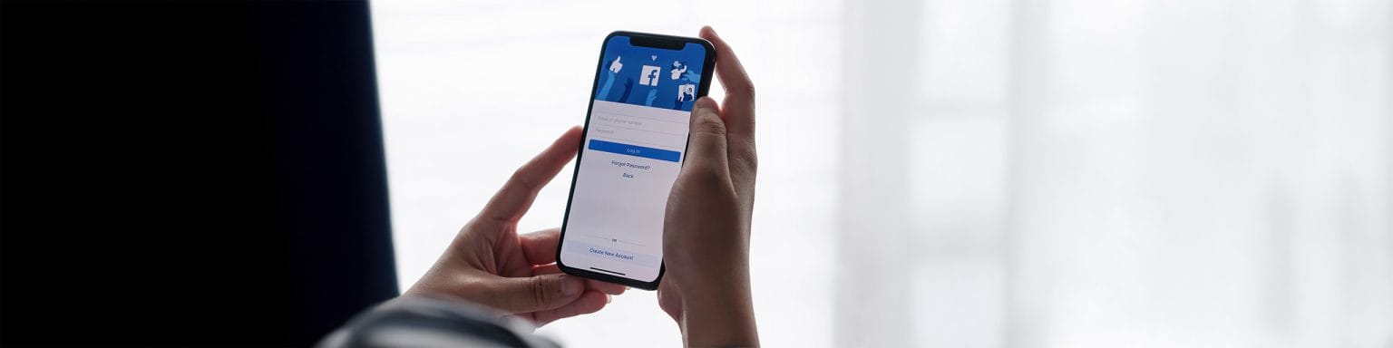 Pantalla de inicio de sesión de Facebook en un iPhone sostenido por una mujer, simbolizando las nuevas penalizaciones por contenido copiado en 2025.